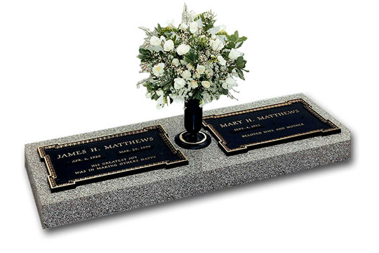 Bronze memorial on granite base with flowers in vase.