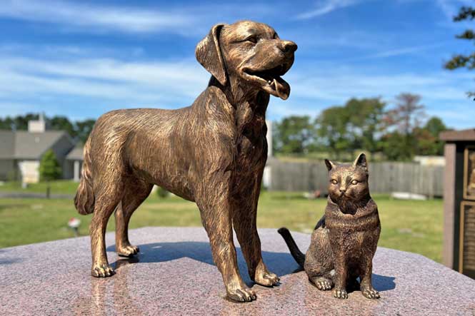 Pet loss services and burial gardens in cemetery with bronze statue of dog and cat.