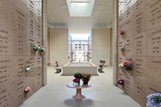 Mausoleum crypts with flowers in vases in the Mausoleum Cloister at Dulaney Valley Memorial Gardens, featuring a skylight and wrought iron gate.