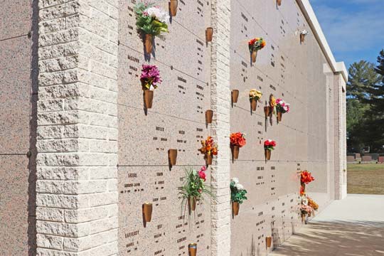 Cremation niches with granite fronts next to mausoleum crypts with vases and flowers.